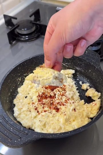 A plate of scrambled eggs mixed with cooked yogurt crumbles and red pepper flakes.