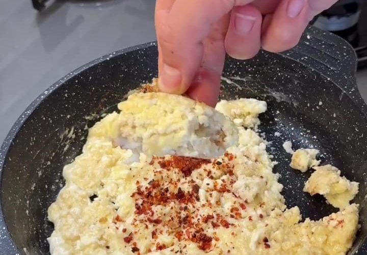 A plate of scrambled eggs mixed with cooked yogurt crumbles and red pepper flakes.