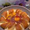 A sizzling breakfast skillet with simit pieces, sucuk, melted cheese, and eggs.