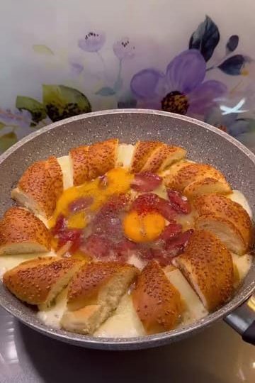 A sizzling breakfast skillet with simit pieces, sucuk, melted cheese, and eggs.