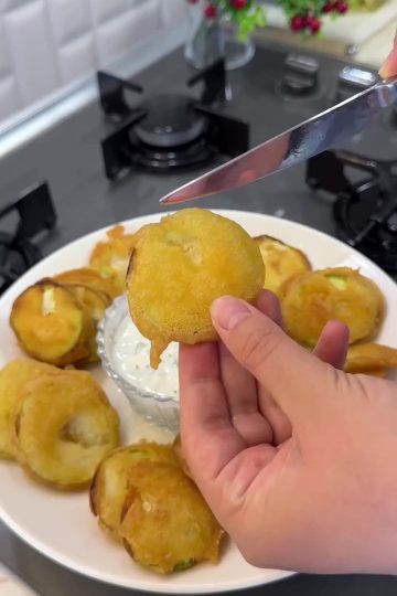 A heap of golden crispy fried zucchini slices on a plate with yogurt dip.