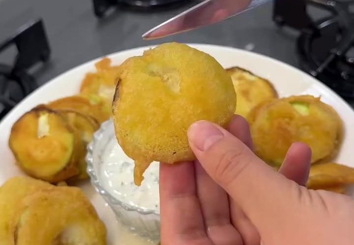 A heap of golden crispy fried zucchini slices on a plate with yogurt dip.