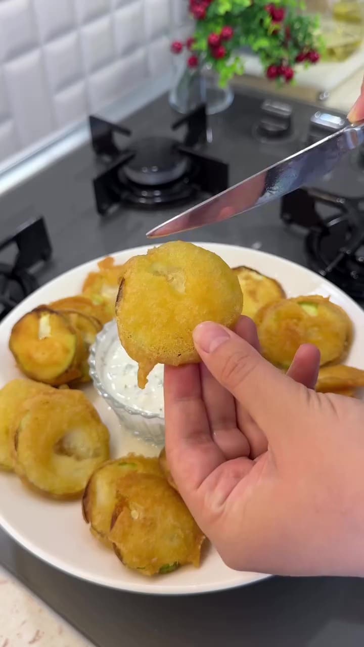 A heap of golden crispy fried zucchini slices on a plate with yogurt dip.