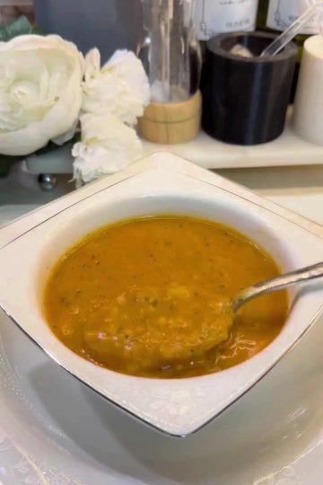 A rustic bowl of Turkish Ezogelin soup garnished with dried mint and a lemon wedge.