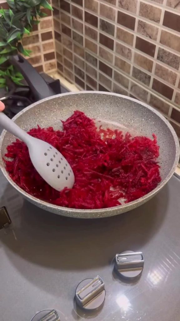 Sautéing grated red beets in a skillet with oil.