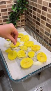 Adding oil and oregano to a layer of sliced potatoes.
