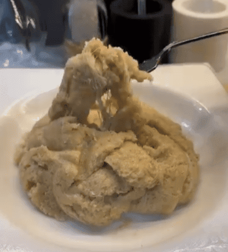 A spoonful of golden semolina halva with long, stretchy melted cheese strands.