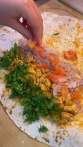 Adding fresh tomatoes and sumac onions to the chicken wrap.