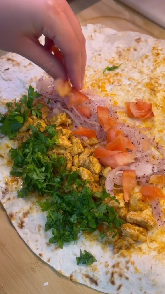 Adding fresh tomatoes and sumac onions to the chicken wrap.