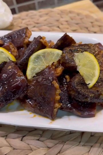 A platter of glossy, dark purple dried eggplant dolmas garnished with fresh herbs.