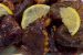 A platter of glossy, dark purple dried eggplant dolmas garnished with fresh herbs.