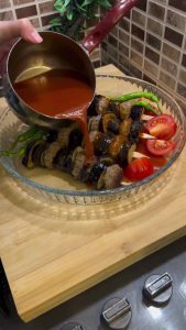 Assembling the eggplant and meatball skewers in a baking dish.