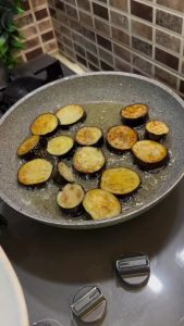 Deep frying sliced eggplant rounds in a skillet until golden brown.