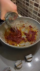 Whisking water into tomato paste to create a savory kebab sauce.