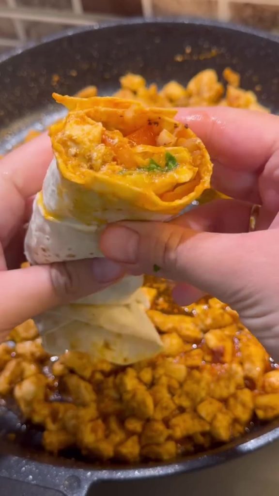 A succulent chicken tantuni wrap with tomatoes, sumac onions, and parsley on a plate.