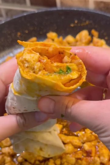 A succulent chicken tantuni wrap with tomatoes, sumac onions, and parsley on a plate.
