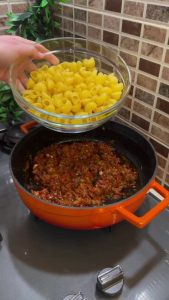 Stirring dry pasta into a savory minced meat and paste base.