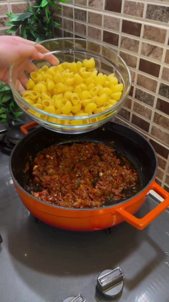 Stirring dry pasta into a savory minced meat and paste base.