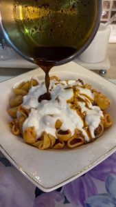 Drizzling red pepper oil over a plate of Turkish Mantı pasta.