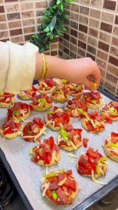 Adding sucuk, peppers, and corn to mini pizza bases.