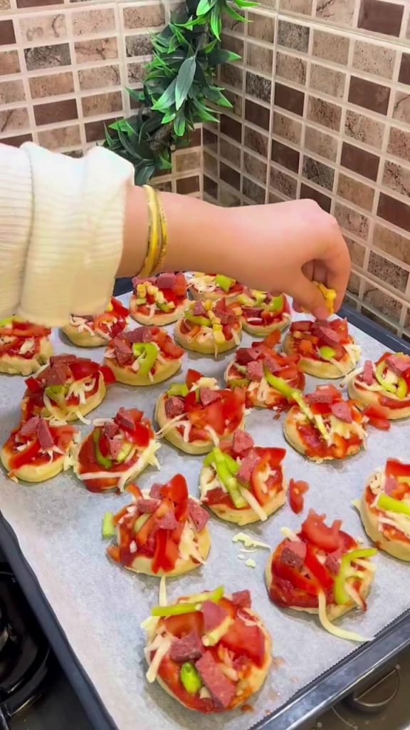 Adding sucuk, peppers, and corn to mini pizza bases.