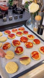 Brushing tomato and oregano sauce over dough circles.