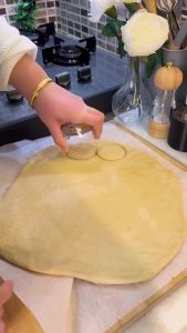 Using a drinking glass to cut circular shapes from pizza dough.