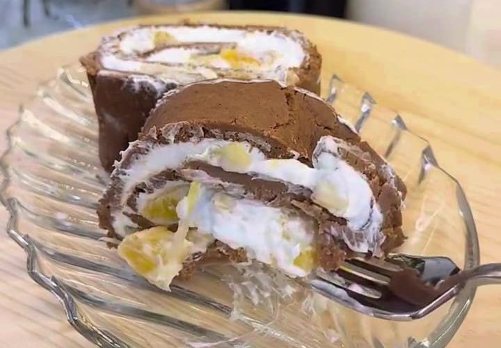 A beautiful sliced biscuit log cake filled with cream and orange pieces.