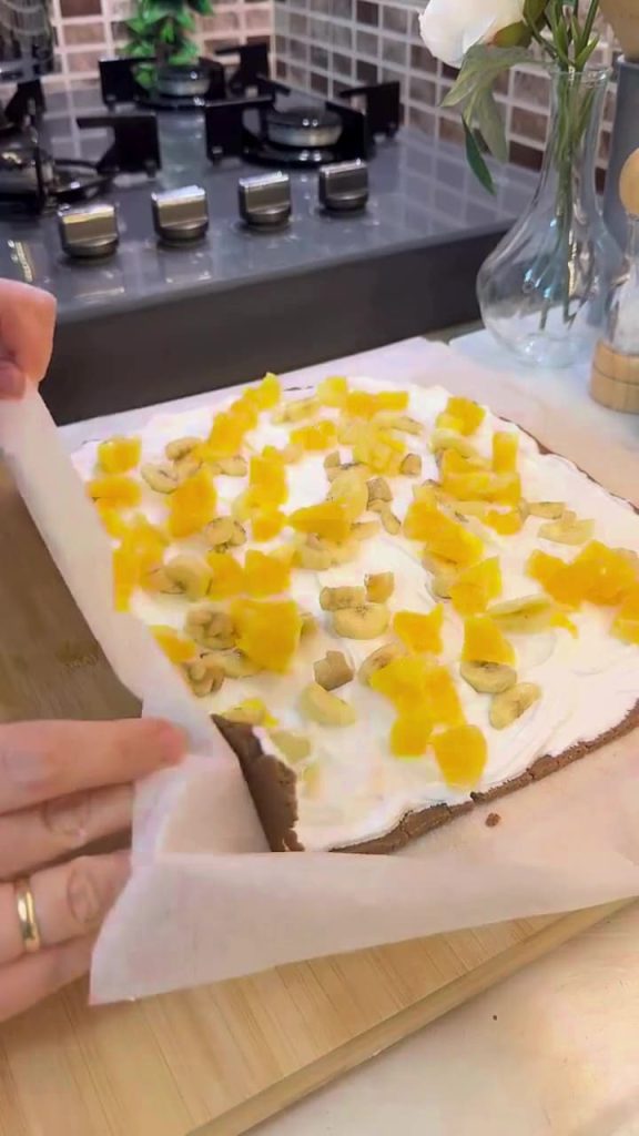 Adding fresh orange and banana pieces to a cream-filled cake.