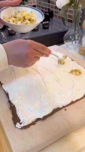 Spreading white whipped cream over a dark biscuit cake base.