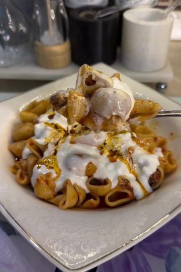 A bowl of meat-sauce pasta topped with thick garlic yogurt and red pepper oil.