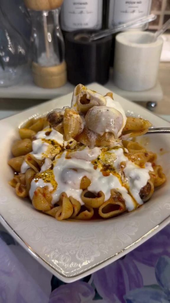 A bowl of meat-sauce pasta topped with thick garlic yogurt and red pepper oil.