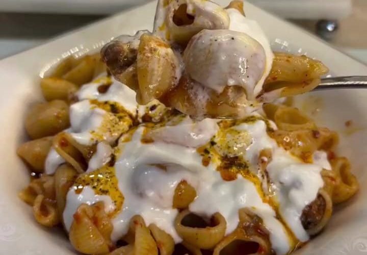 A bowl of meat-sauce pasta topped with thick garlic yogurt and red pepper oil.