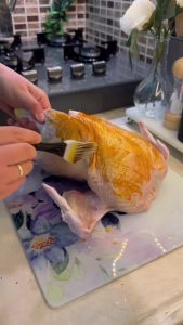 Brushing red paprika oil rub over a whole chicken.