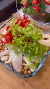 Adding boiled chickpeas and vegetables to a baking dish.
