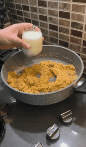Pouring milk into a pot of roasted semolina.