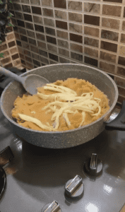 Adding shredded string cheese to a hot pot of halva.
