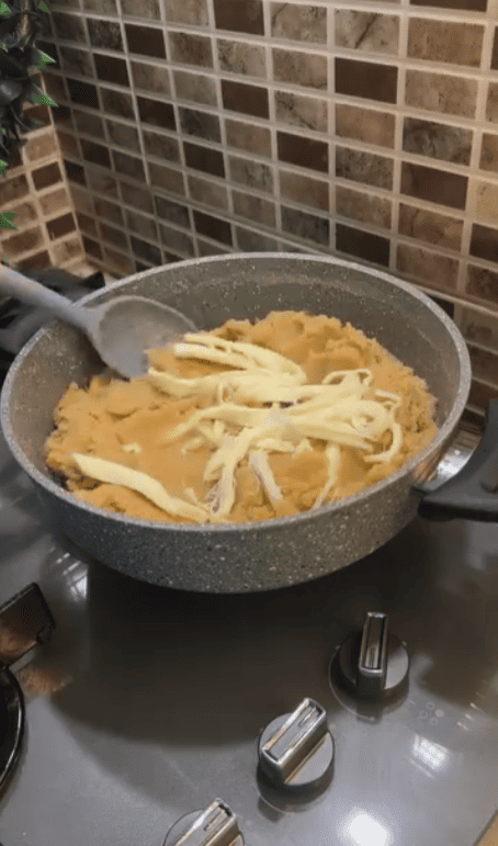 Adding shredded string cheese to a hot pot of halva.