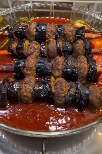 A professional presentation of Turkish eggplant and meatball skewers in a baking dish.