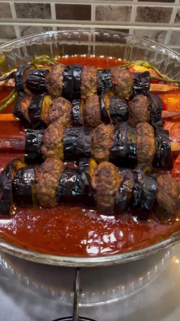 A professional presentation of Turkish eggplant and meatball skewers in a baking dish.