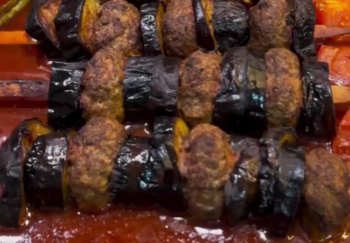 A professional presentation of Turkish eggplant and meatball skewers in a baking dish.