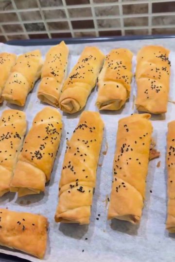 A tray of golden brown, crispy Turkish cheese böreks with nigella seeds.