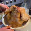 A golden-brown whole roasted chicken sitting upright in a bundt cake pan.