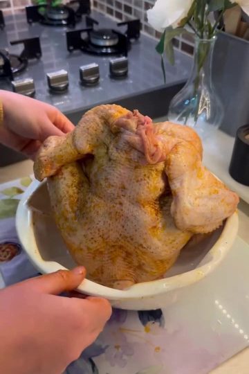 A golden-brown whole roasted chicken sitting upright in a bundt cake pan.