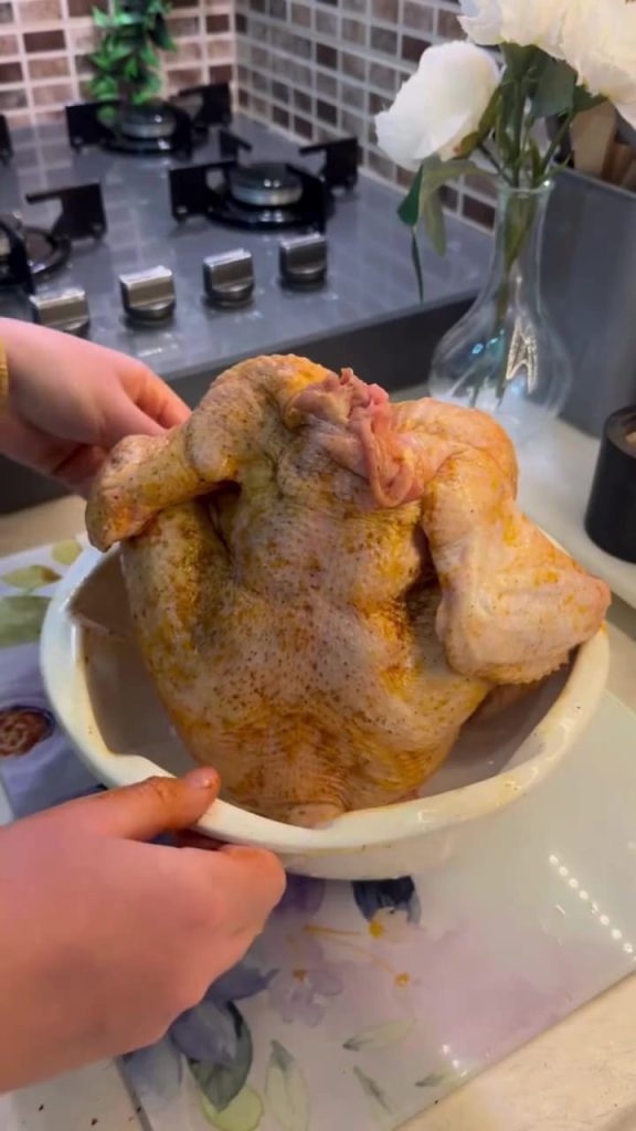 A golden-brown whole roasted chicken sitting upright in a bundt cake pan.