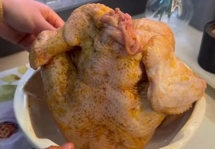 A golden-brown whole roasted chicken sitting upright in a bundt cake pan.