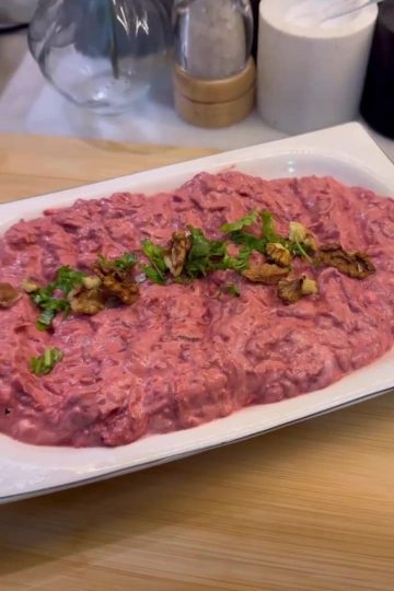 A bowl of electric pink beetroot meze topped with walnuts and parsley.