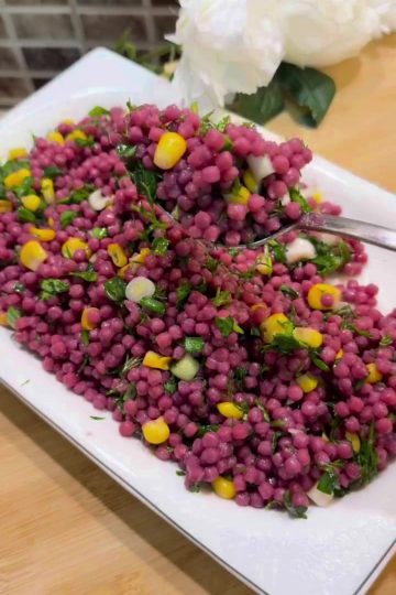 A large bowl of bright purple Turkish couscous salad with corn and fresh herbs.