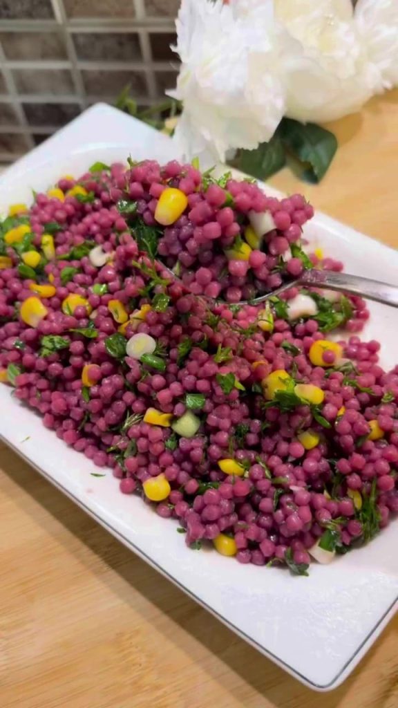 A large bowl of bright purple Turkish couscous salad with corn and fresh herbs.