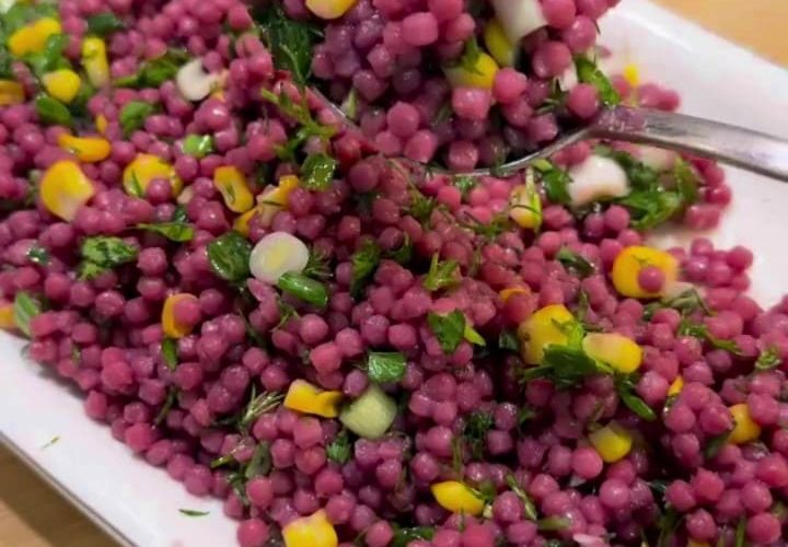 A large bowl of bright purple Turkish couscous salad with corn and fresh herbs.